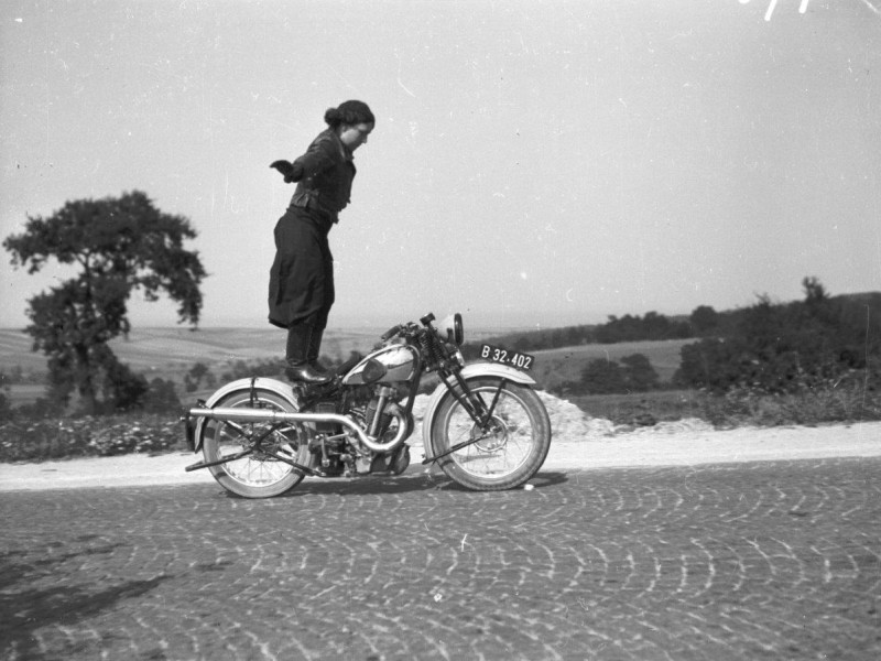 A black and white photo of Anny Deim standing on a riding motorbike: 
